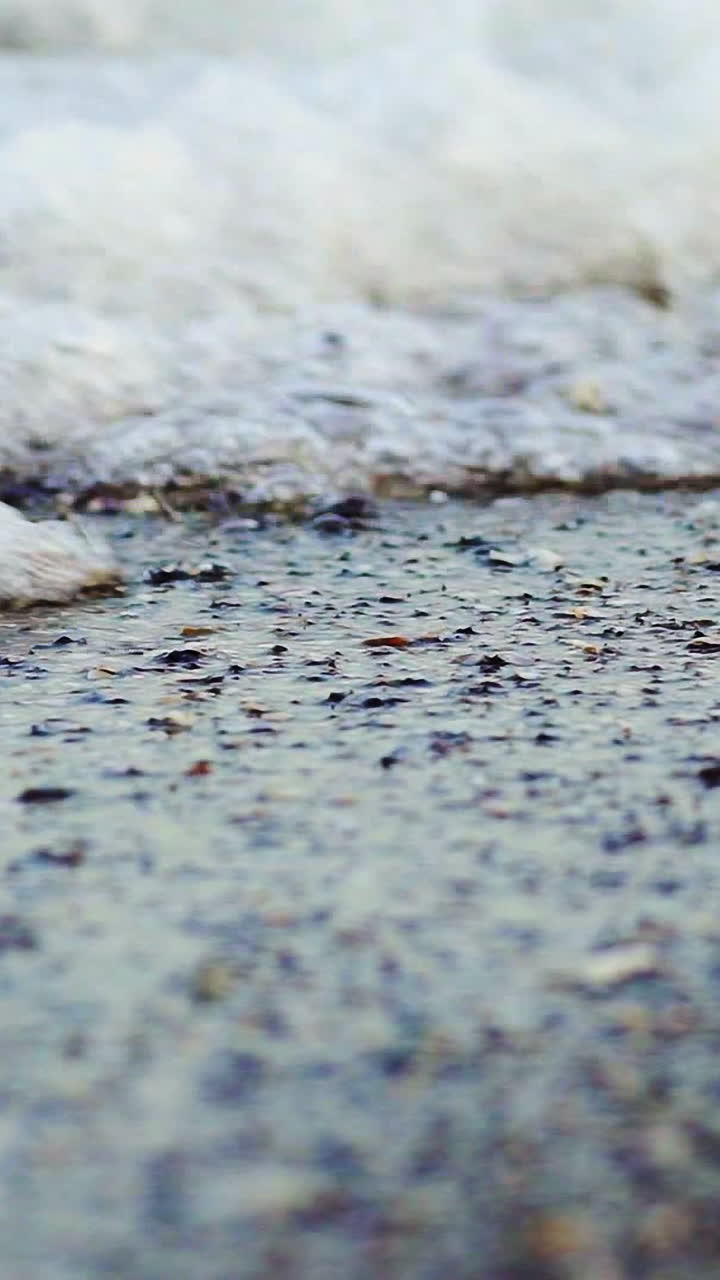 Foamy sea shore at the beach. Close up view of soft waves lapped the sandy beach. Vertical video