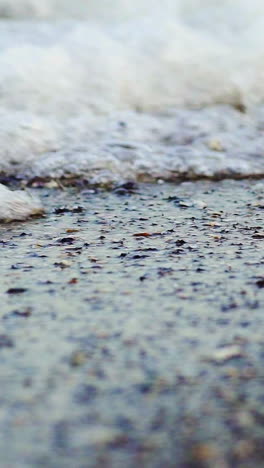 foamy sea shore at the beach. close up view of soft waves lapped the sandy beach. vertical video