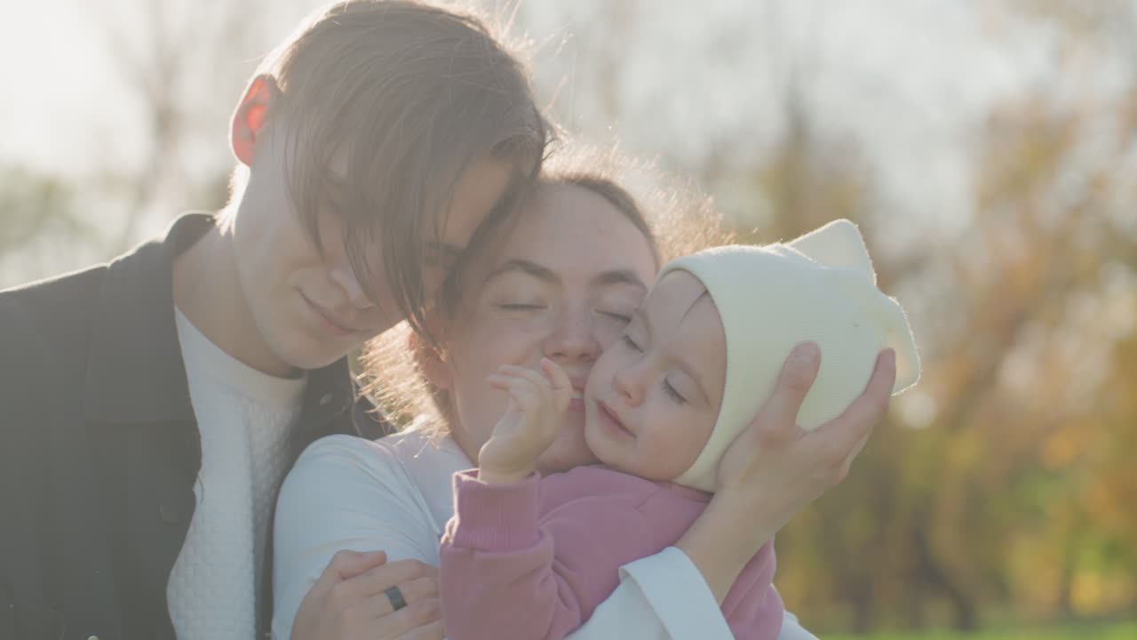 Ritratto di famiglia gioioso. Immagine spontanea di una famiglia allegra che si abbraccia all'aperto sotto la luce del sole. Momento spontaneo catturato di una famiglia felice che scambia gesti affettuosi sotto una luce solare splendente