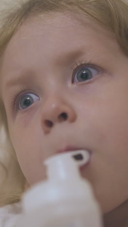 troubled little blonde girl undergoes procedure with inhaler lying in comfortable bed at home extreme close view