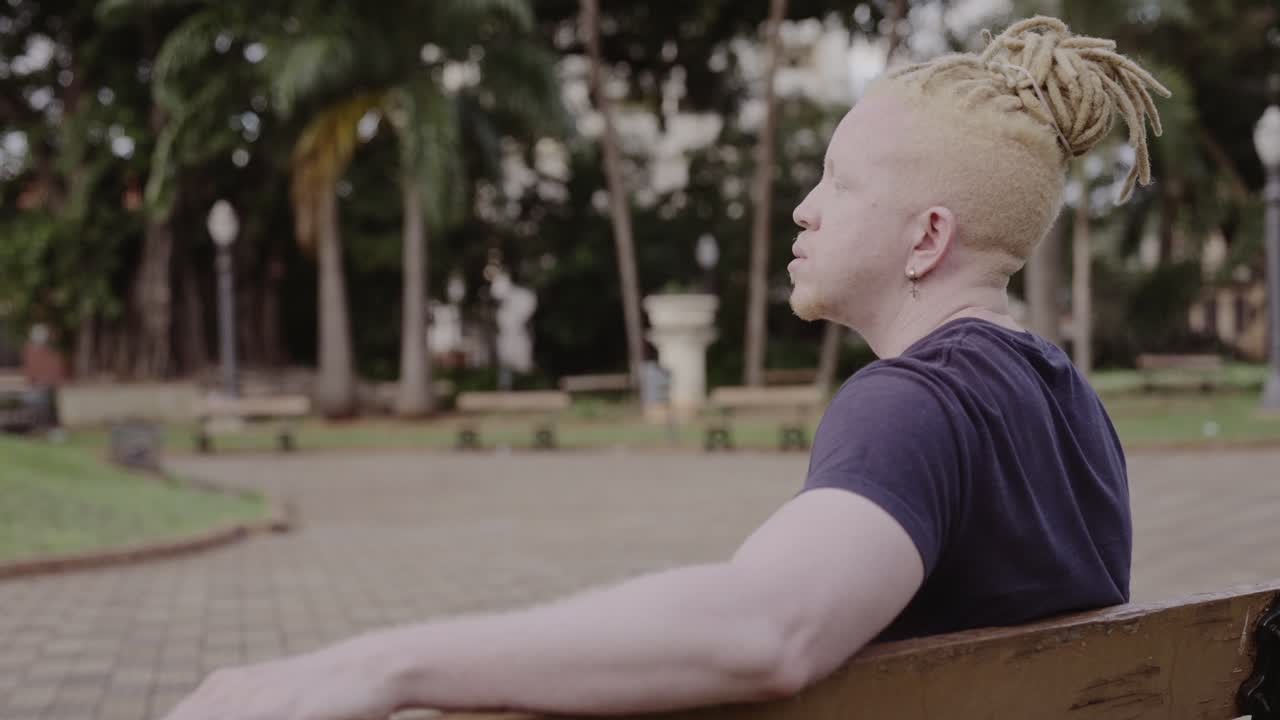 Man with blonde dreadlocks sitting on a park bench