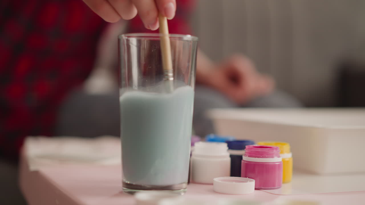 женщина в красной рубашке моет кисть в стекле, делая картинку эбру