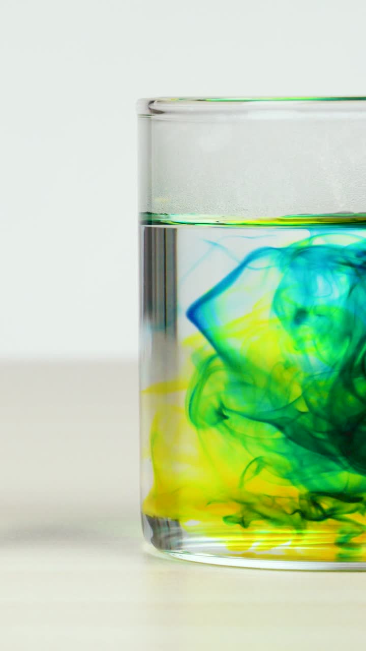 Colorante alimentare giallo e blu vivace turbina e si diffonde all'interno di un contenitore di vetro trasparente.