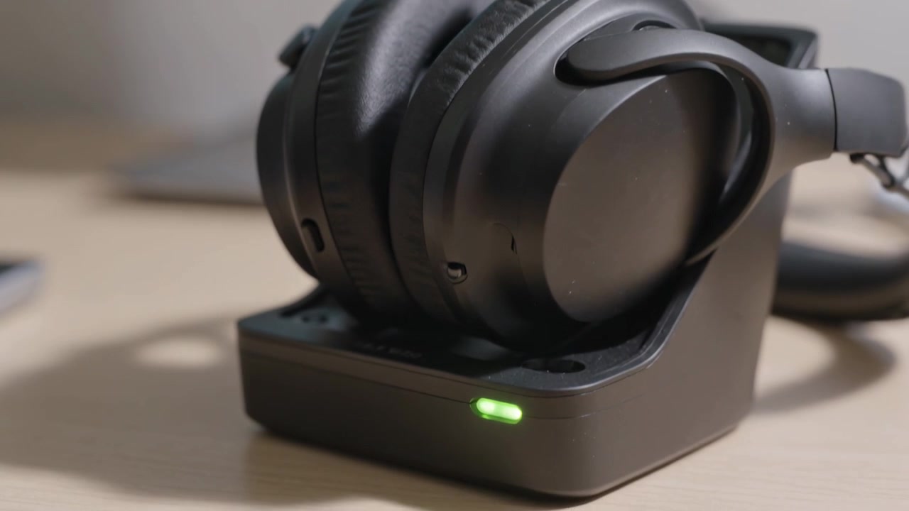 Powering compact dock lighting green LED and charging folded black over-ear headphones on wood desk