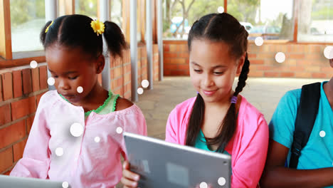 Animation-of-floating-dots-over-diverse-girls-using-digital-tablet-in-classroom-at-school