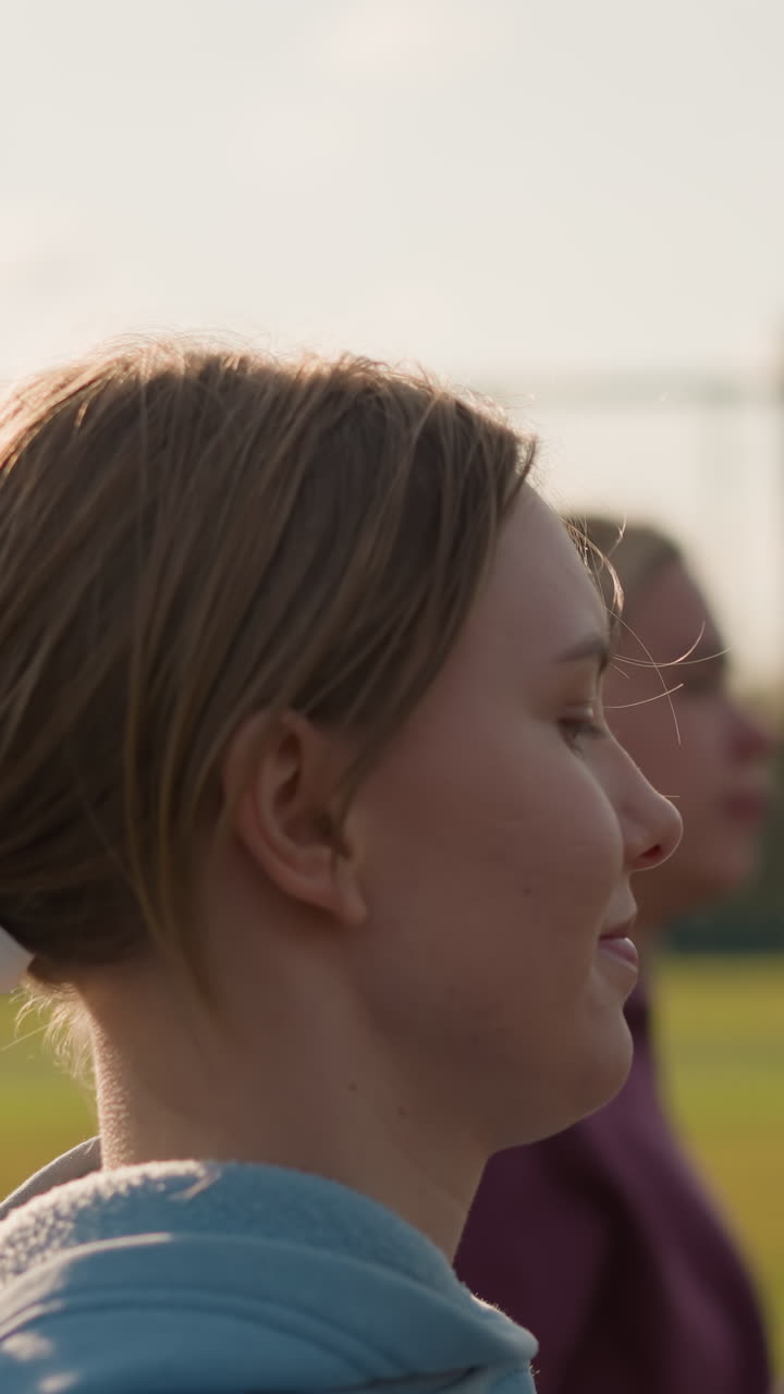 Primo piano di un giovane che salta durante un'intensa sessione di allenamento di pallavolo con la rete davanti, con la luce del sole che si riflette sui capelli; sullo sfondo si intravede un impianto sportivo all'aperto