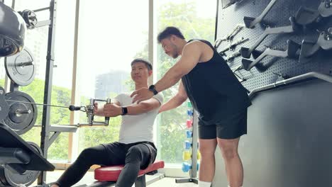 a trainer guides a client through a seated cable row exercise in a well-lit gym setting