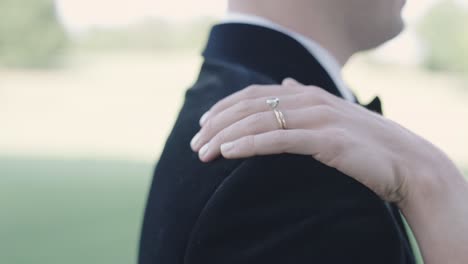 bride's hand with wedding ring moving up groom's arm from elbow to shoulder