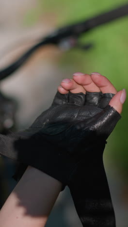 primer plano de un individuo de pie al lado de la bicicleta, desabrochando la correa del guante de motociclista con atención cuidadosa, mientras que el fondo muestra vegetación borrosa