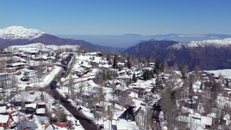 Dolly-in-flyover-of-cabins-and-houses-made-of-wood-and-local-stone-and-establishing-in-the-snow-filled-village-of-Farellones,-Chile