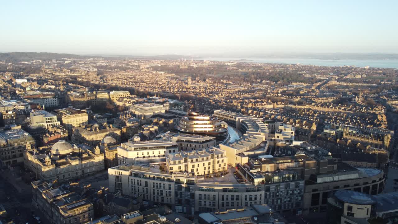 Drone captures Edinburgh St James Quarter and nearby architecture bathed in soft golden sunlight with detailed city layout, rooftops, and distant coast showing modern and historic blend in Scotland
