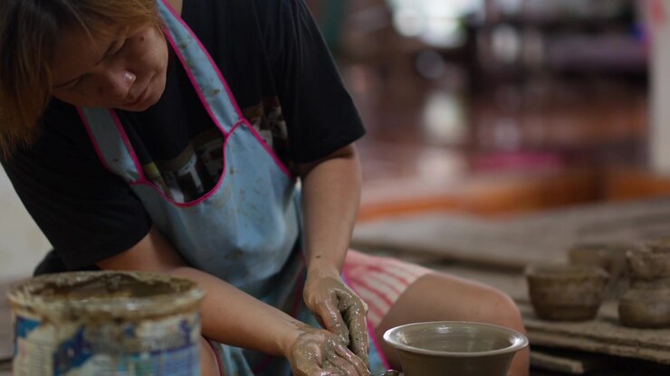 An Asian female potter shapes wet clay pottery on a spinning wheel in Nonthaburi, Thailand.
