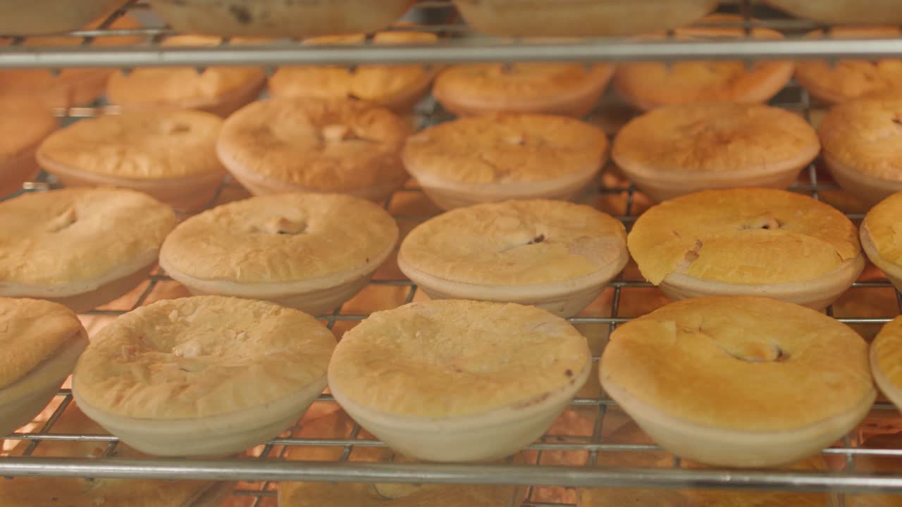 Golden meat pies warm under glass in a well-lit bakery display, camera slowly panning