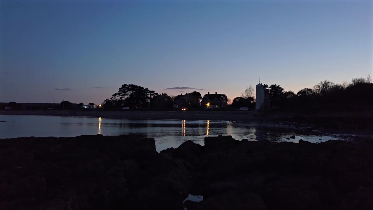 Static wide shot of Isle of Wight beach at dusk with calm water lights