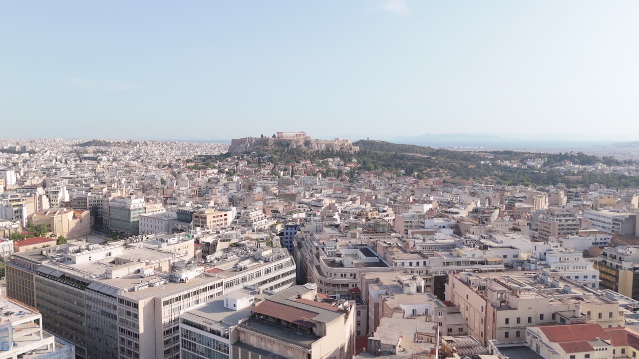 Blue sky above sprawling Athens cityscape with layered rooftops and morning atmosphere, panoramic establishing aerial at midday