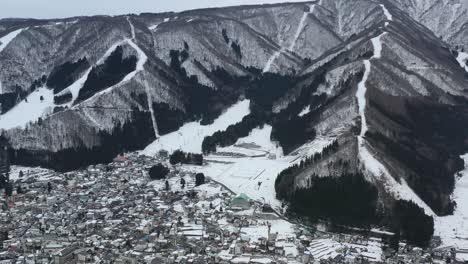 Panorámica-Aérea-Por-El-Pequeño-Pueblo-Debajo-De-La-Estación-De-Esquí-De-Montaña-En-Invierno