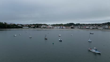 Aerial-flying-over-boats-on-coast-of-Ares,-heading-towards-city,-Spain