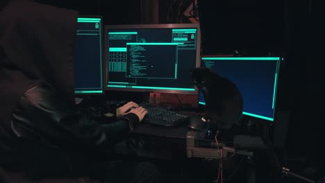 un hacker con un cappuccio si siede davanti agli schermi dei computer e hacker database