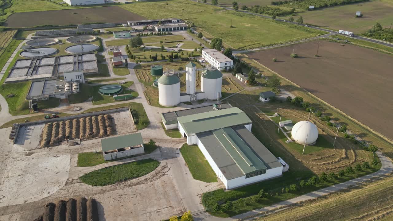 Fly around a modern wastewater treatment plant combined with a biogas production unit. The facility includes sedimentation tanks, green-roofed buildings and fermentation silos.