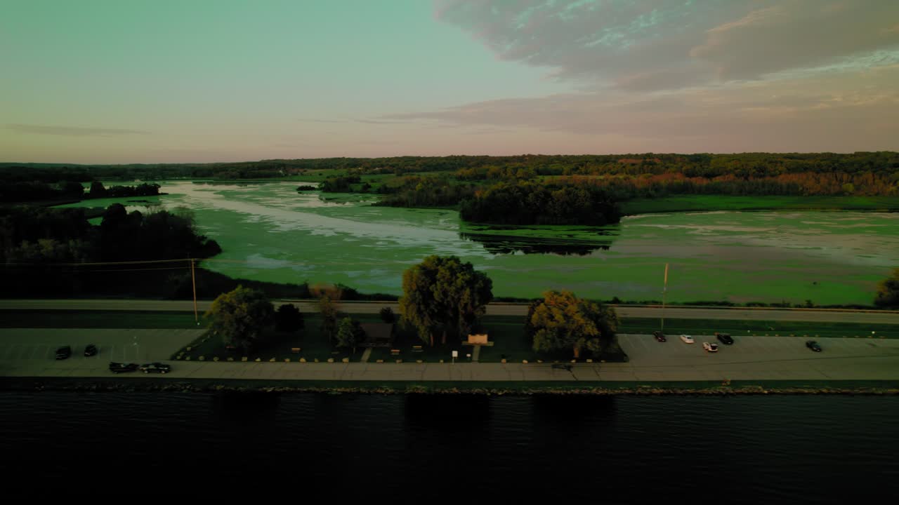 Aerial view of a red car driving near the Green Lake Inlet Boat Launch Site in Ripon, Wisconsin, with a serene water landscape in the background. Peaceful travel along the lakeside.
