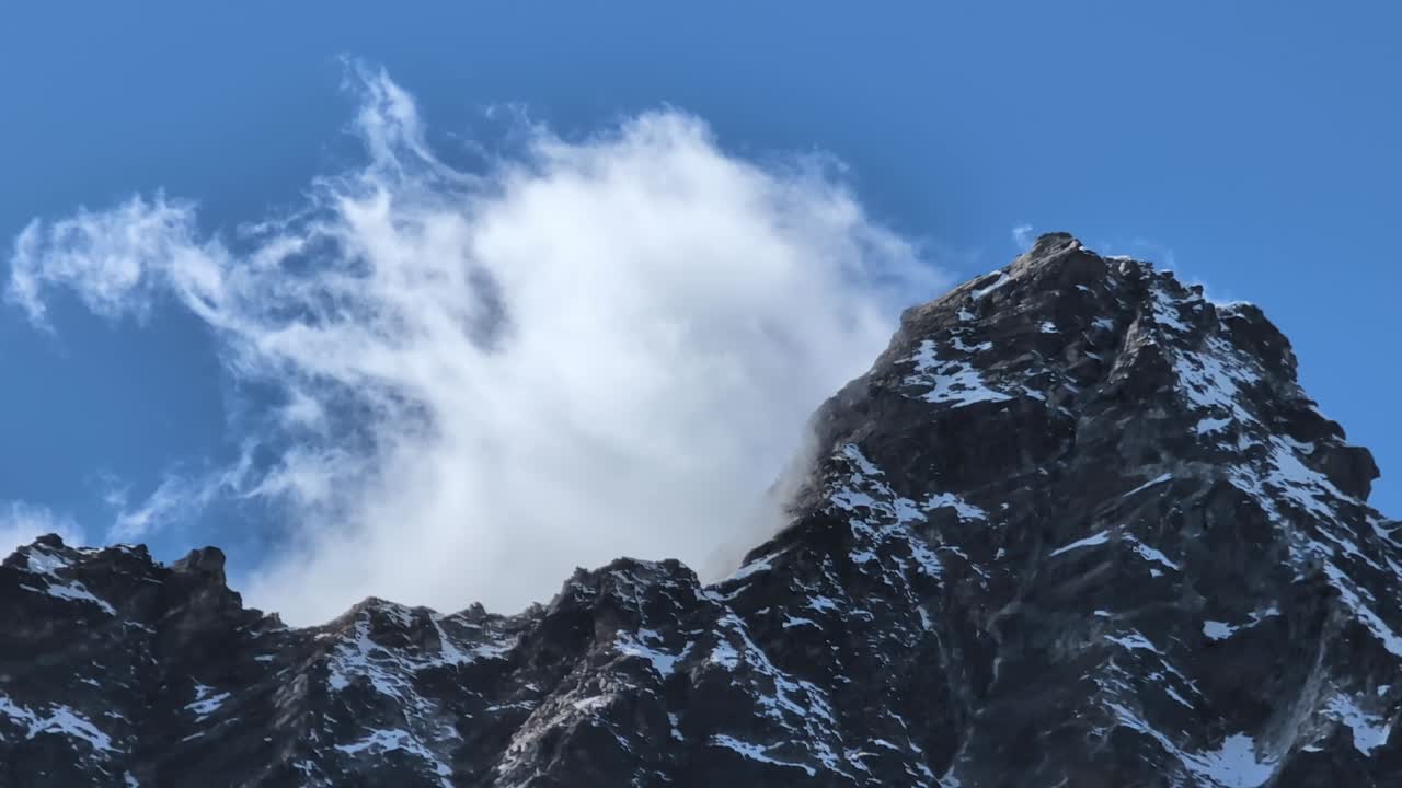 웅장한 히말라야 산꼭대기의 클로즈업 뷰: 하 구름이 극적으로 갈라져서 정상이 드러나고 높은 고도에서 자연의 역동적인 힘을 보여줍니다.