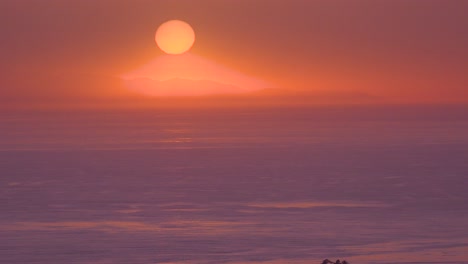 a huge red round ball of sun at sunset over the pacific ocean near malibu, california