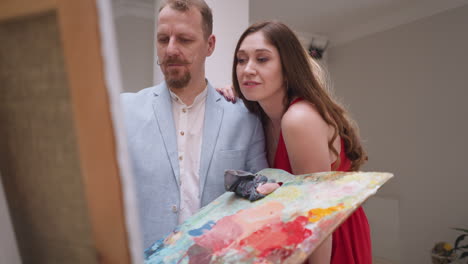 woman model puts arm on artist shoulder. emotional connection forged through model and bearded artist shared artistic endeavors. creator and muse