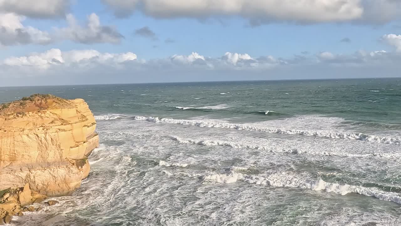 Dynamic ocean waves crash against rugged cliffs under a partly cloudy sky, showcasing nature's raw beauty.