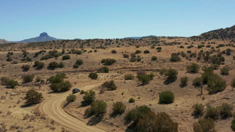 Antena-Siguiendo-El-Coche-Por-Un-Camino-De-Tierra-Con-Curvas-En-Un-Paisaje-Desértico