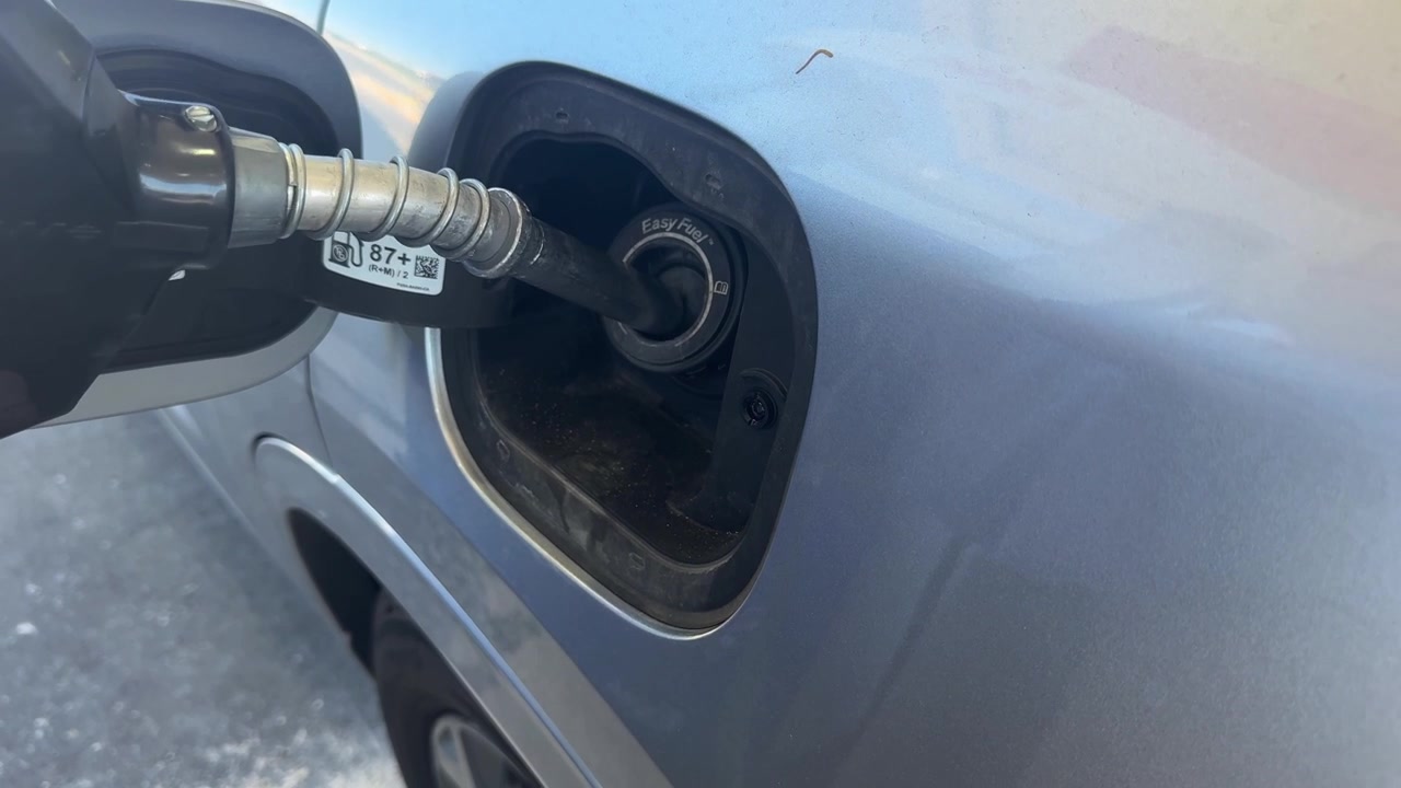 A gas nozzle is inserted into the car’s fuel filler neck during refueling. This is the vehicle’s fueling opening, and the nozzle is positioned inside it to transfer fuel.