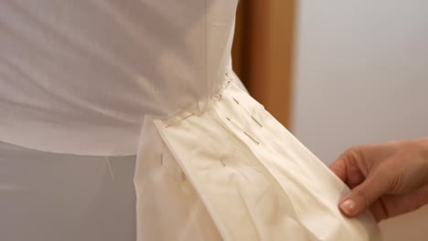 hands of fashion designer fine tuning a wedding bride dress train with needles on manikin, close up