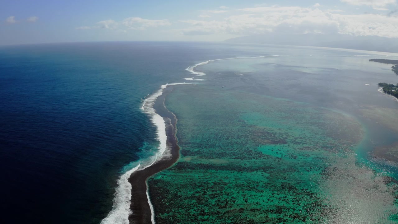 Prise de vue aérienne par drone au-dessus du récif corallien de Teahupoo, Tahiti, un horizon pacifique brumeux où la mer et le ciel se confondent au-delà des hauts-fonds du lagon turquoise.