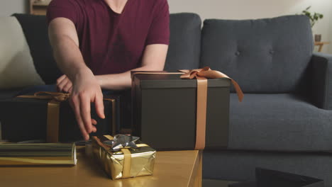 close up of man gift wrapping presents on table at home with wrapping paper sticky tape and scissors