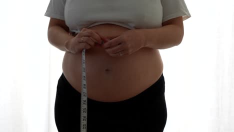 pregnant woman rolls tape after measuring her belly at 38 weeks in soft daylight