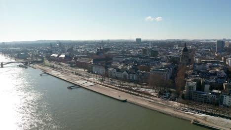 Drone-flight-towards-a-snowy-Mainz-the-City-of-Biontech-on-a-sunny-Winter-day-showing-flood-of-the-Rhine-river-and-blue-sky