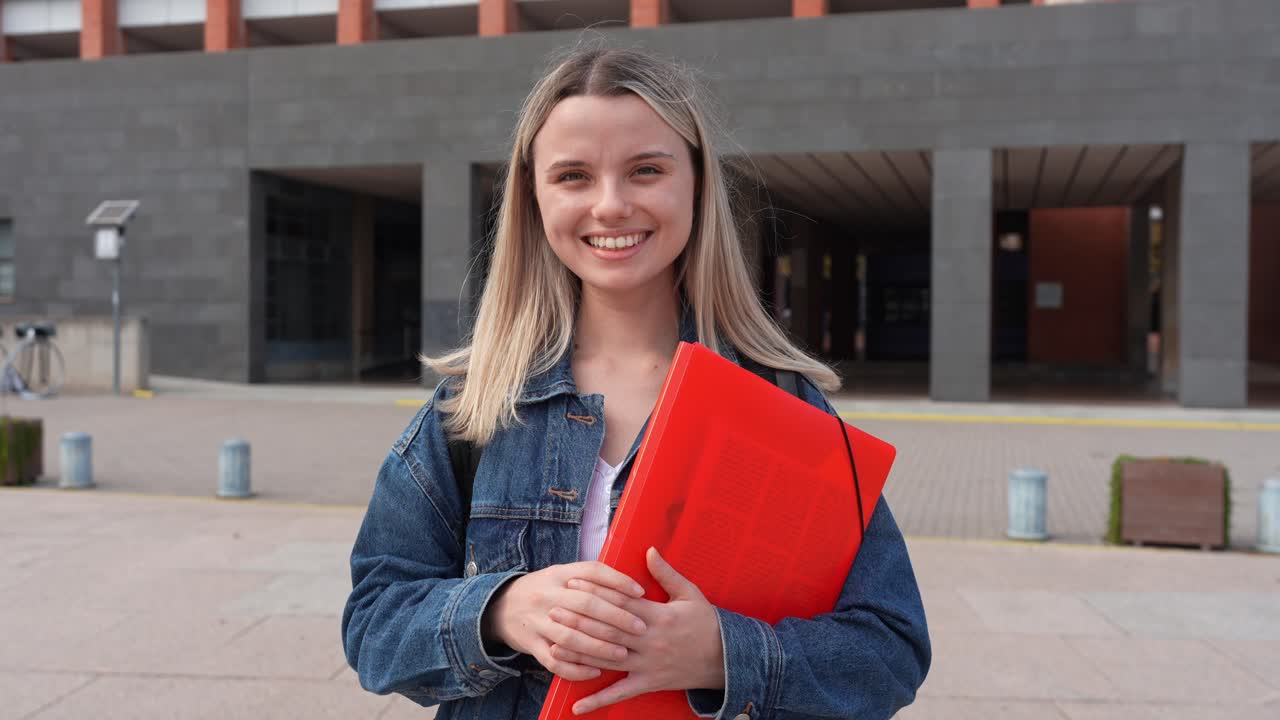 Giovane studentessa sorridente con cartella rossa nel campus universitario