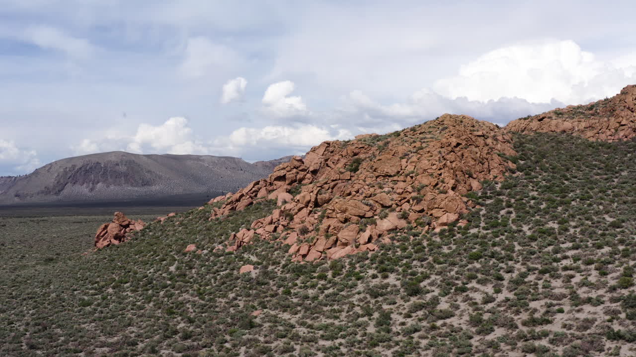 cresta de montaña de cráter con formaciones de roca roja distintivas y vegetación escasa contra un telón de fondo de montañas y cielo en los buttes eolianos