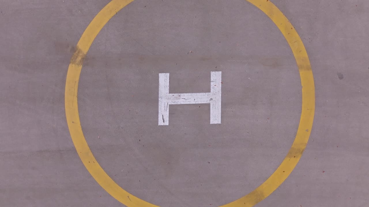 Aerial top-down view of a helipad with bold yellow circle and white "H" marking on concrete surface. Ideal for aviation, transportation, and infrastructure content