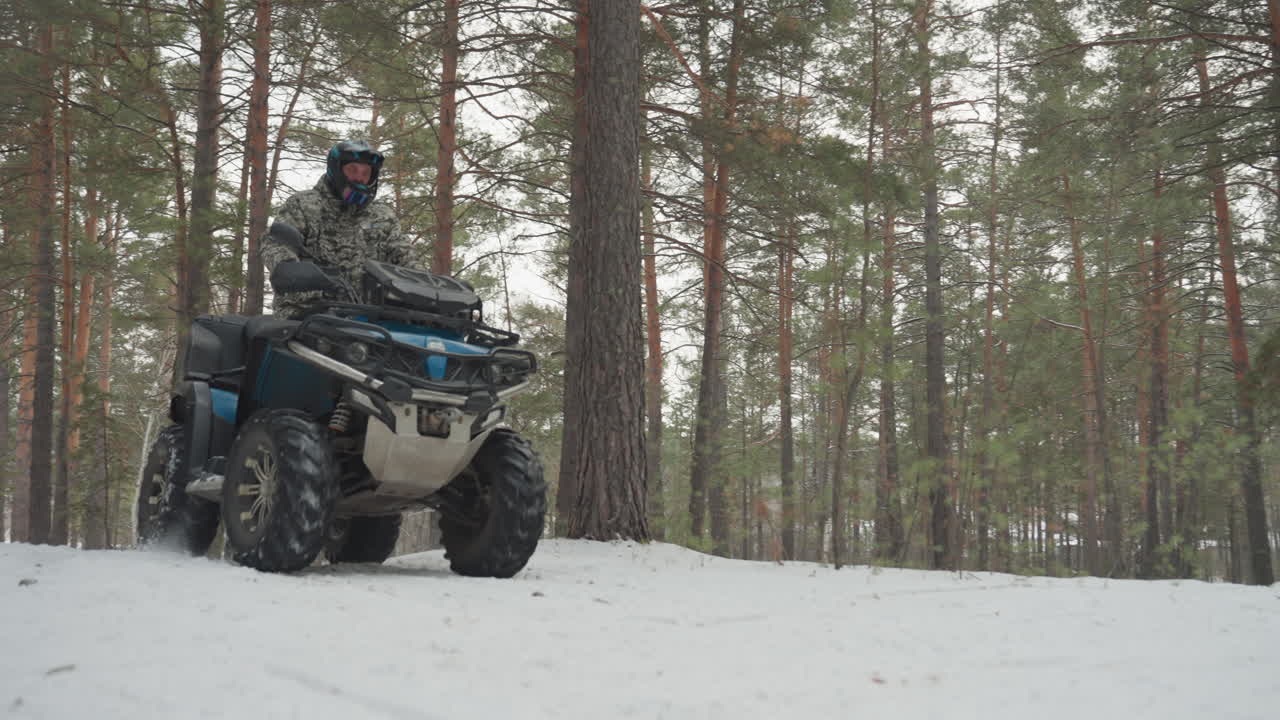 Un pilota di ATV nella foresta innevata si muove energicamente tra i pini silenziosi, un singolo pilota su un quad blu naviga un sentiero innevato, una telecamera ad angolo basso mostra pneumatici robusti che sollevano neve, un pilota con casco in tuta isolante, cielo coperto.