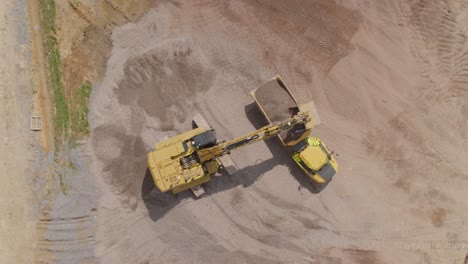 una excavadora carga grava en un camión de basura en un gran sitio de construcción