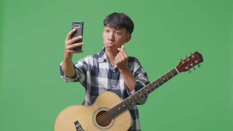녹색 화면 배경에 서 있는 스마트폰에서 기타 셀피를 찍은 아시아 십대