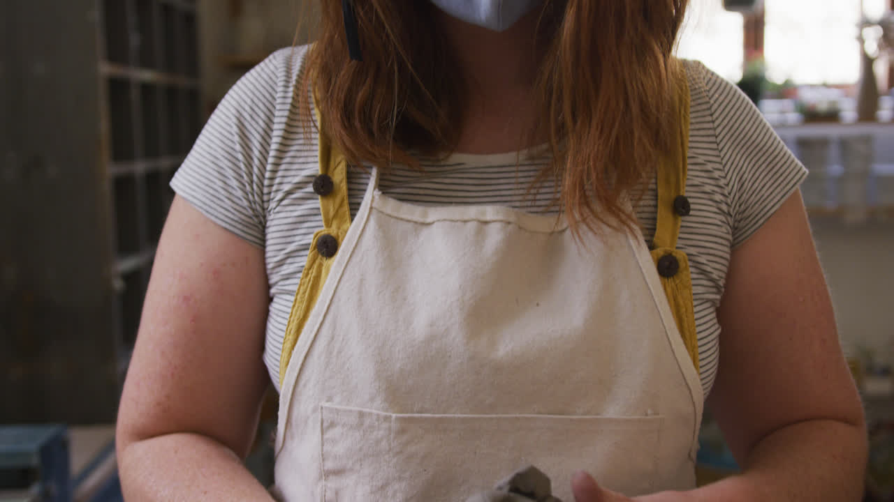Portrait of female potter wearing face mask and apron working on clay at pottery studio