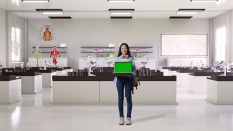 full body of asian teen girl student with a backpack smiling and showing green screen laptop to camera while standing in science laboratory