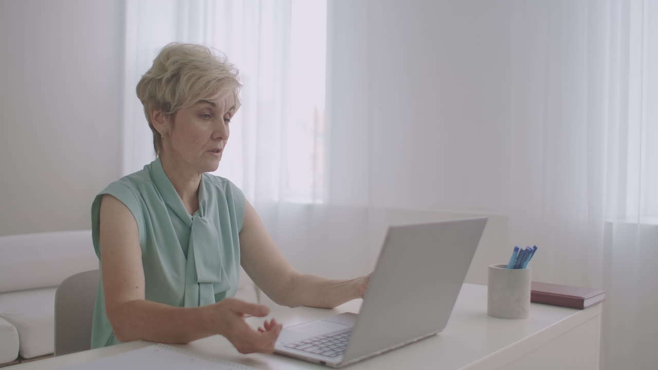 aged female teacher is lecturing online looking at web camera of laptop distant education by internet portrait of woman