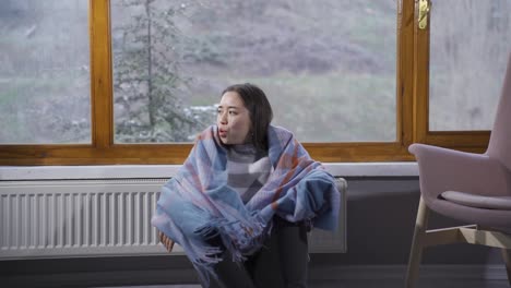 겨울에 집에서 추운 젊은 아시아 여성이 몸을 따뜻하게 하려고 노력하고 있습니다.