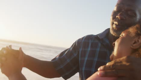una pareja afroamericana de alto nivel sonriendo tomados de la mano y bailando en una playa soleada