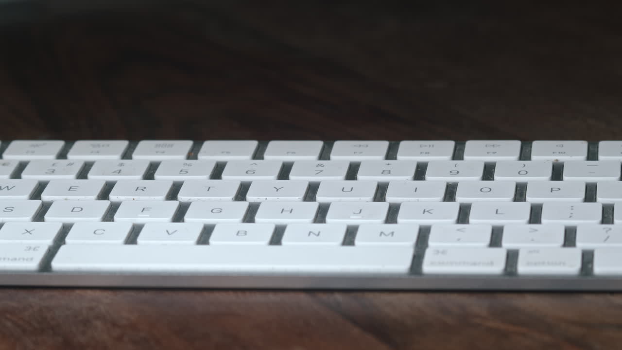 teclado blanco sobre una mesa de madera en una habitación oscura, paralaje lento