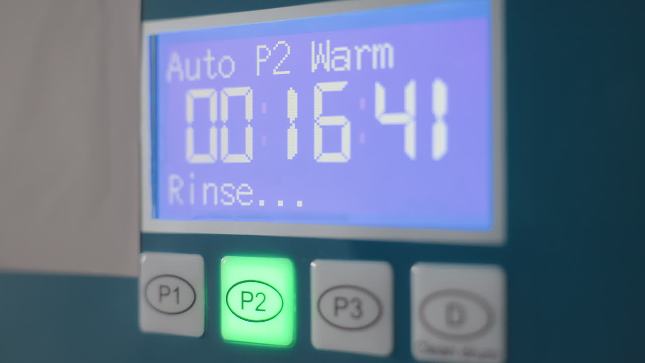 Close up laundry machine indicator with P2 green light, digital timer 00:16:45 warm rinse mode on control panel, illuminated button on stainless washer in laundromat, equipment, clear display UI