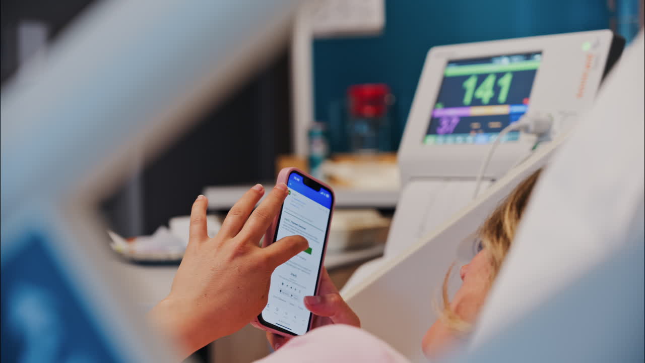 Chisinau, Moldova - May 31, 2025: Pregnant woman using the iHerb app on her phone while doing a prenatal check-up at the doctor's office