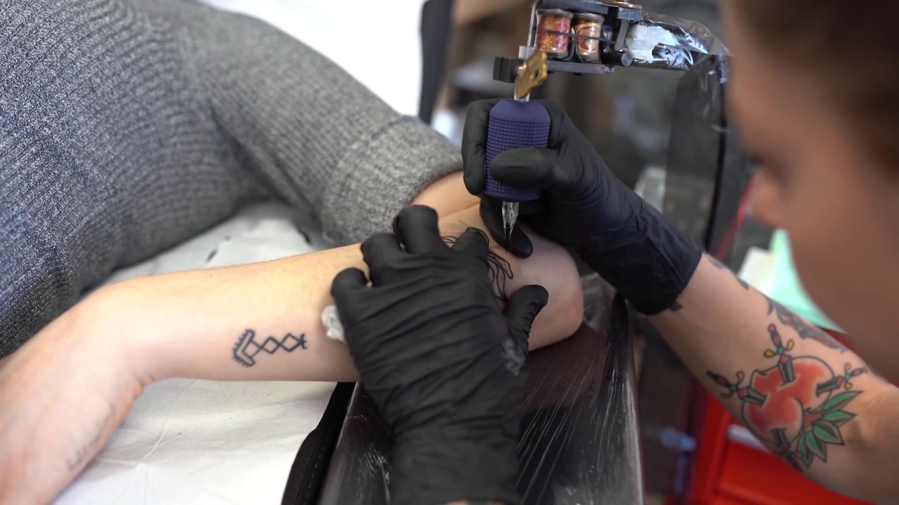 Tatuatrice che tatua una pesca sul braccio di una donna